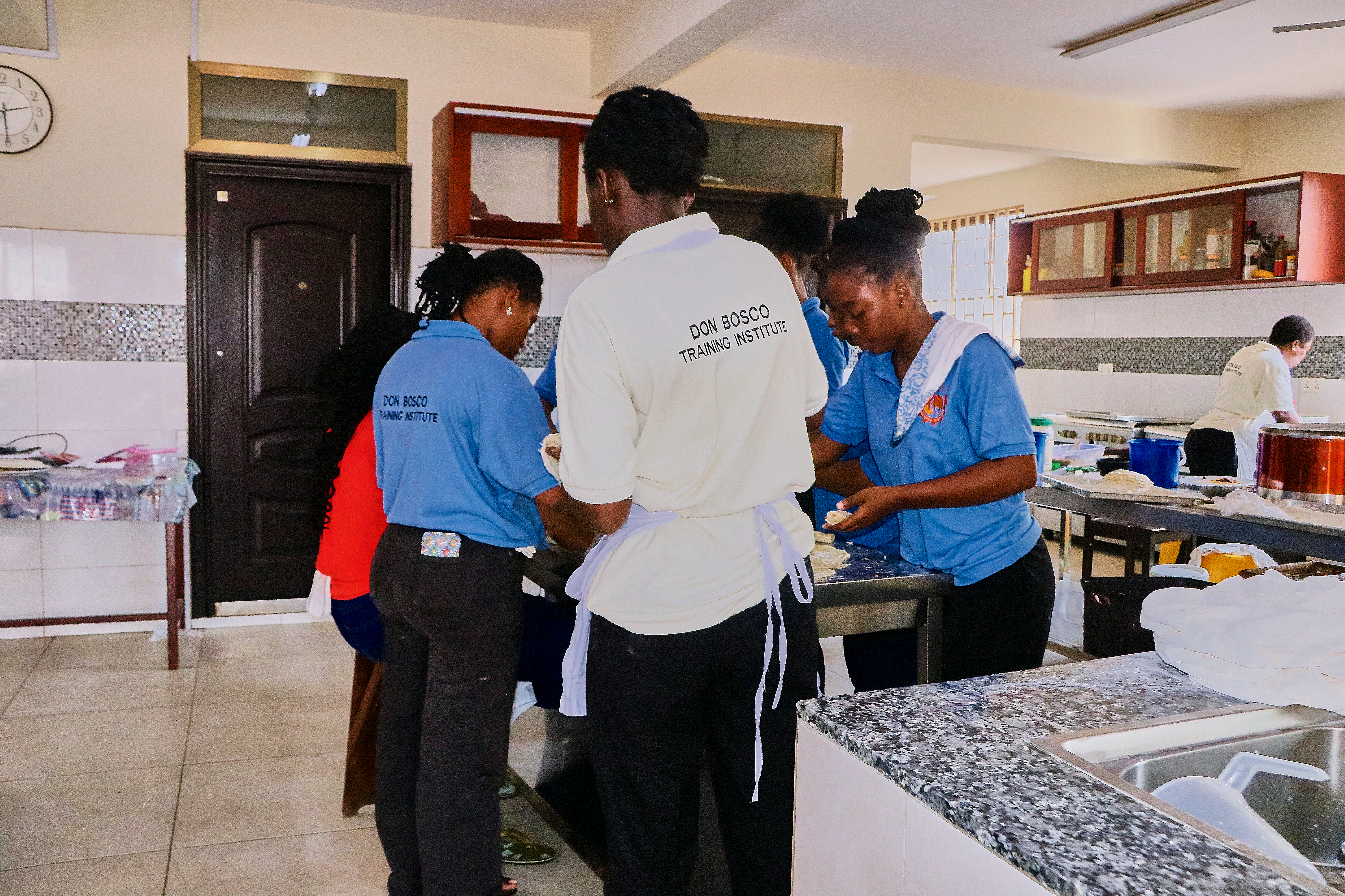 Hospitality trainees in DBTI polo uniforms preparing dough and culinary items in commercial kitchen